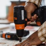 Hands using an orange cordless drill on a workbench