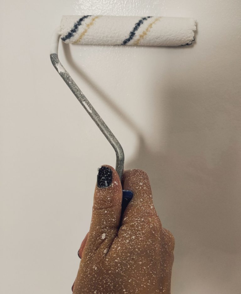 Hand holding a paint roller against a wall